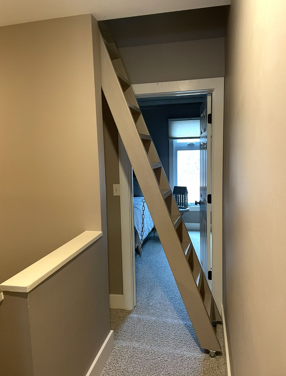A narrow hallway with a wooden staircase leading to a bedroom.
