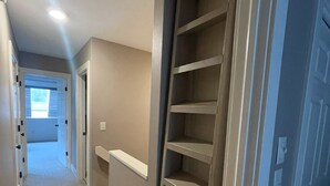 Un couloir doté d’une bibliothèque intégrée, d’un sol recouvert de moquette et d’une porte donnant sur une autre pièce.