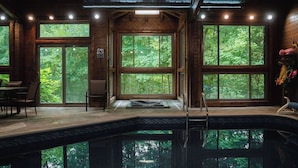 Une cabane en bois dotée d’un grand espace piscine avec de larges baies vitrées, d’un coin salon avec une table et des chaises, et offrant une vue sur la forêt environnante.