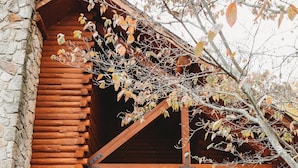 Une cabane en rondins avec une façade en pierre, une véranda en bois et des marches menant à l’entrée.