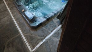 Un bain à remous dans un chalet en bois doté de grandes fenêtres donnant sur une forêt.
