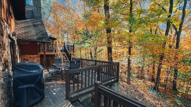 Une terrasse en bois avec des meubles d’extérieur, un barbecue couvert et une cheminée en pierre.