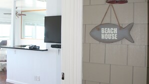 Una zona de cocina con un letrero con forma de pez que dice "BEACH HOUSE" y un farol colgante.
