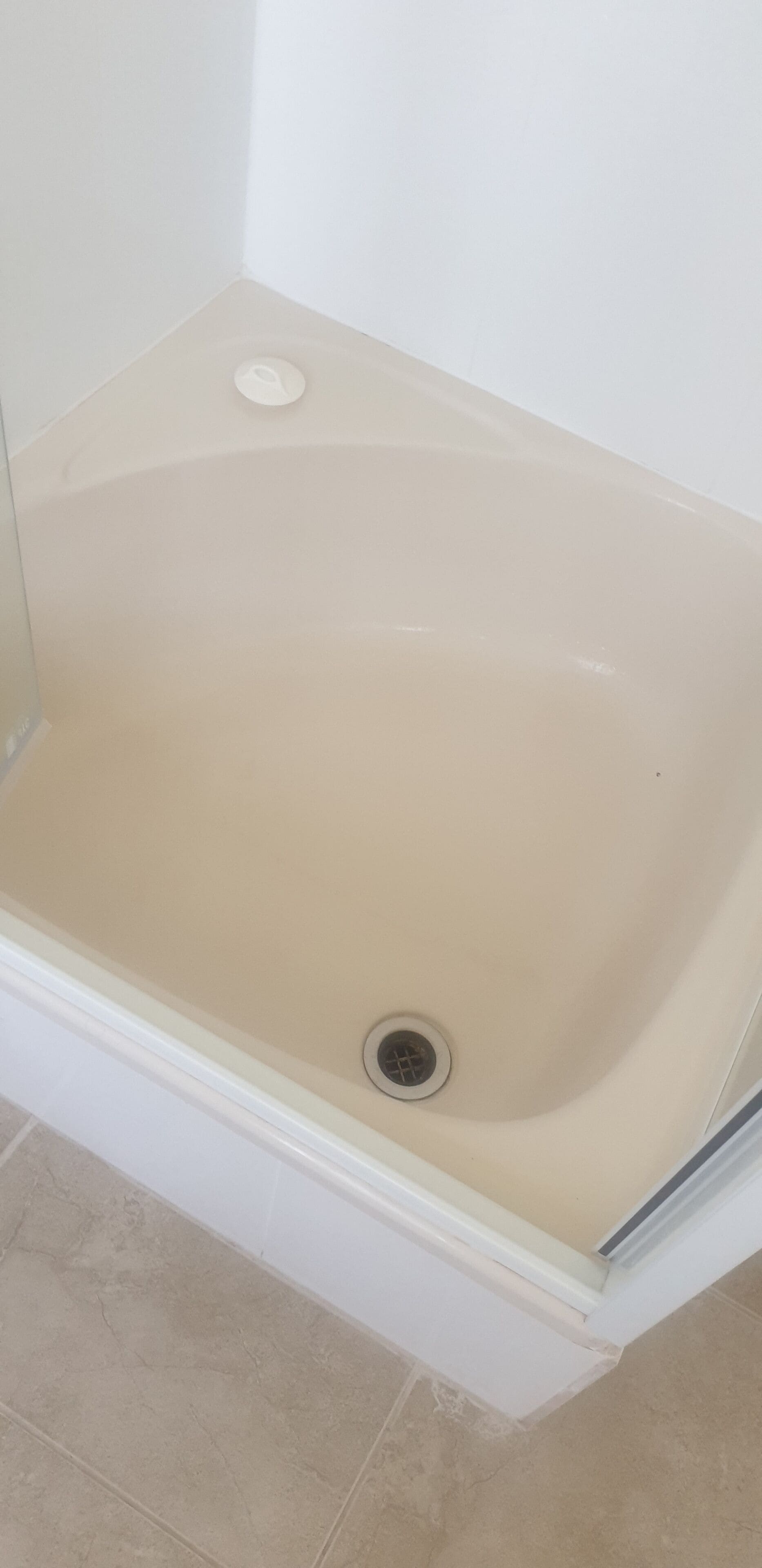 A bathtub with a drain in a corner of a room with white walls and beige tiles.