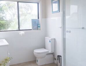 A modern bathroom with a toilet, a shower, and a window with a view of trees.
