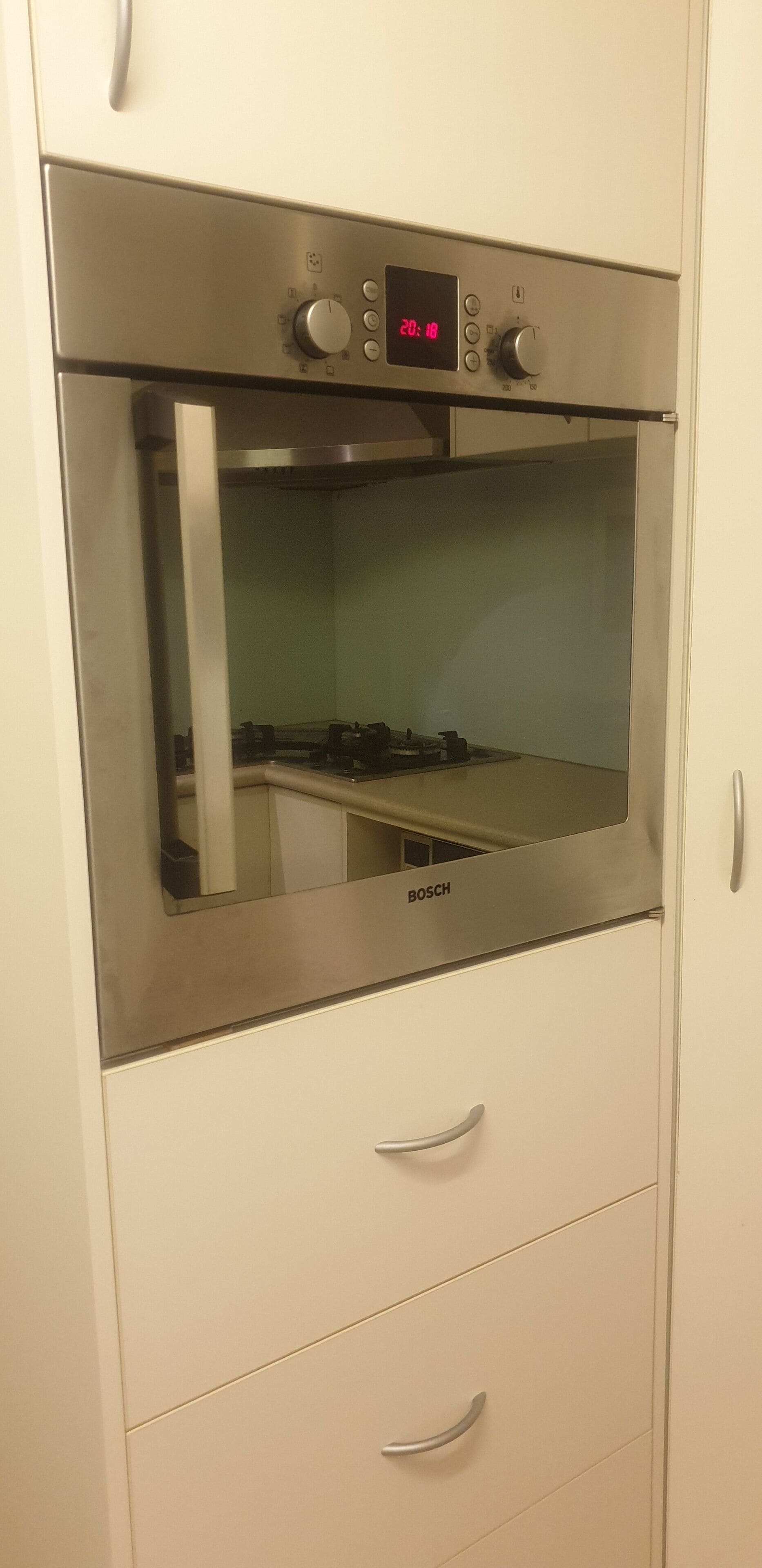 Ein in ein weißes Küchenschränkchen integrierter, edelstahlfarbener Bosch-Backofen mit Digitalanzeige und Bedienknöpfen.