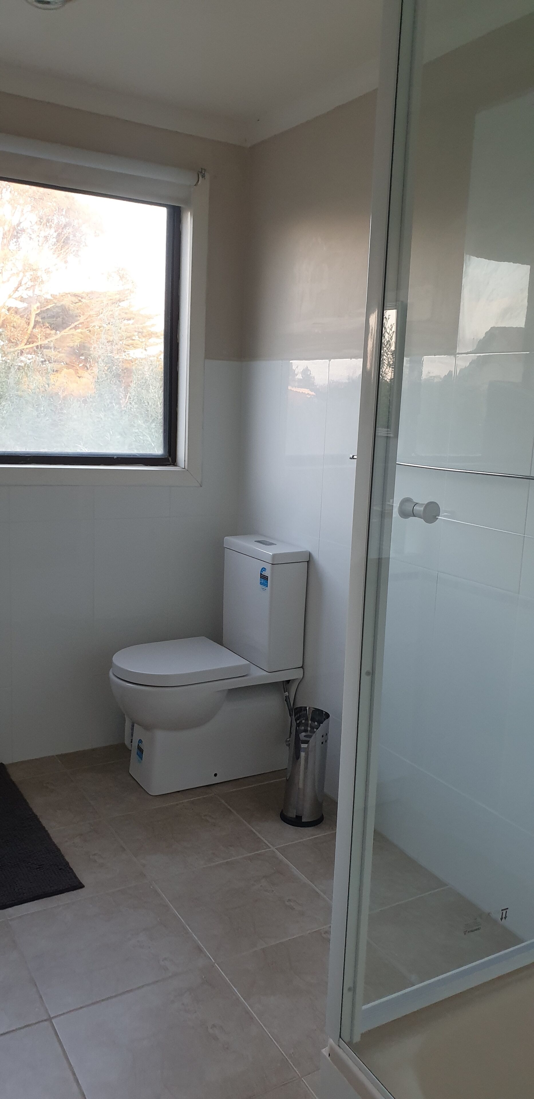 Un baño con inodoro, cabina de ducha de vidrio y ventana.