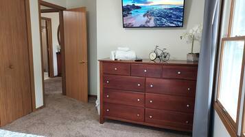 Une chambre à coucher comprenant un lit, une commode, un téléviseur diffusant un paysage pittoresque, et une porte donnant sur une autre pièce.