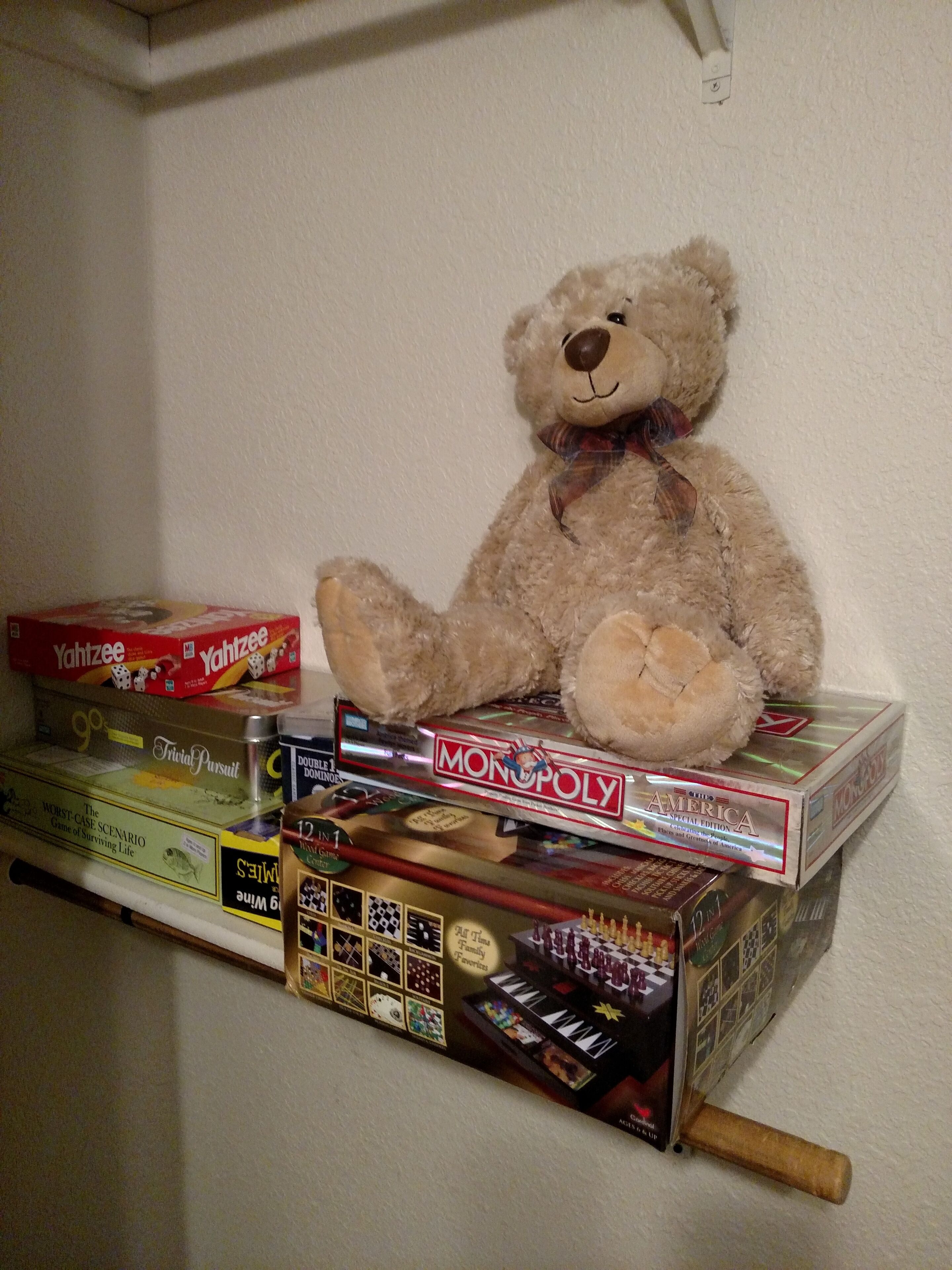 A shelf with various board games and a teddy bear.