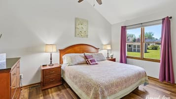 Une chambre à coucher avec un lit en bois, deux lampes de chevet, un ventilateur de plafond, une fenêtre avec des rideaux et une vue sur l’extérieur.