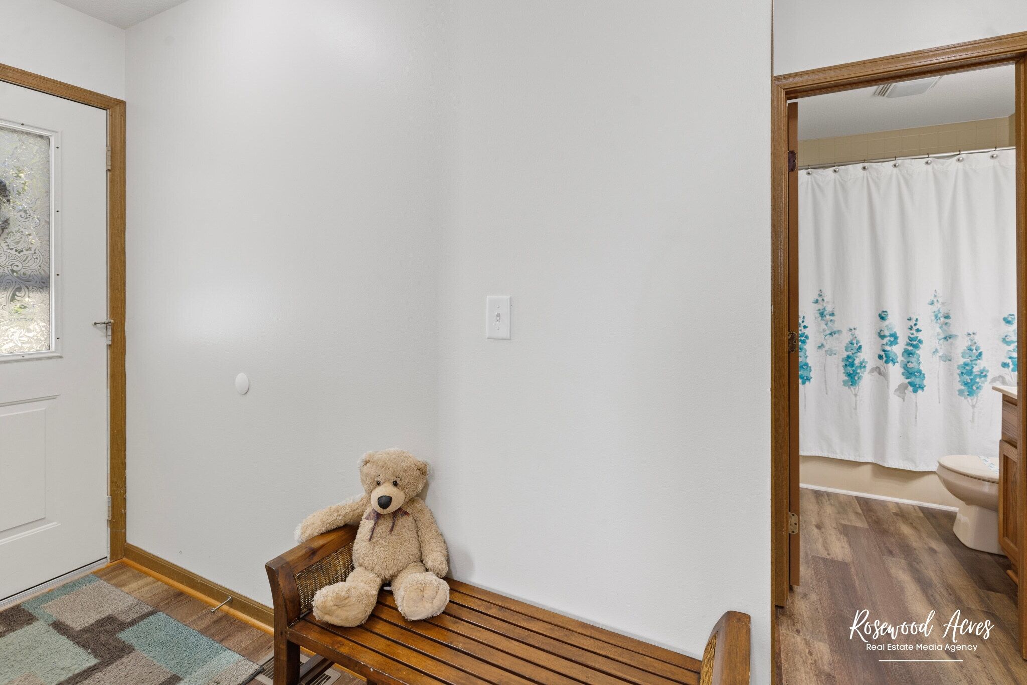A room with a wooden bench, a white door, and a bathroom visible through an open door.