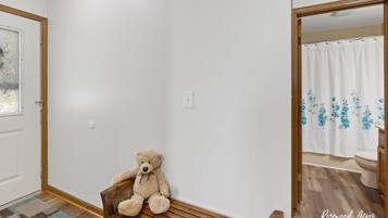 A room with a wooden bench, a white door, and a bathroom visible through an open door.