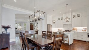 A spacious dining area with a large wooden table and chairs, white cabinetry, and pendant lighting. - Heated Pool Access | 5*Clean | Flex Cancelation (Savannah)