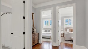 A hallway with a white door, a wooden cabinet, a bed with a white headboard, and a ceiling fan. - Heated Pool Access | 5*Clean | Flex Cancelation (Savannah)