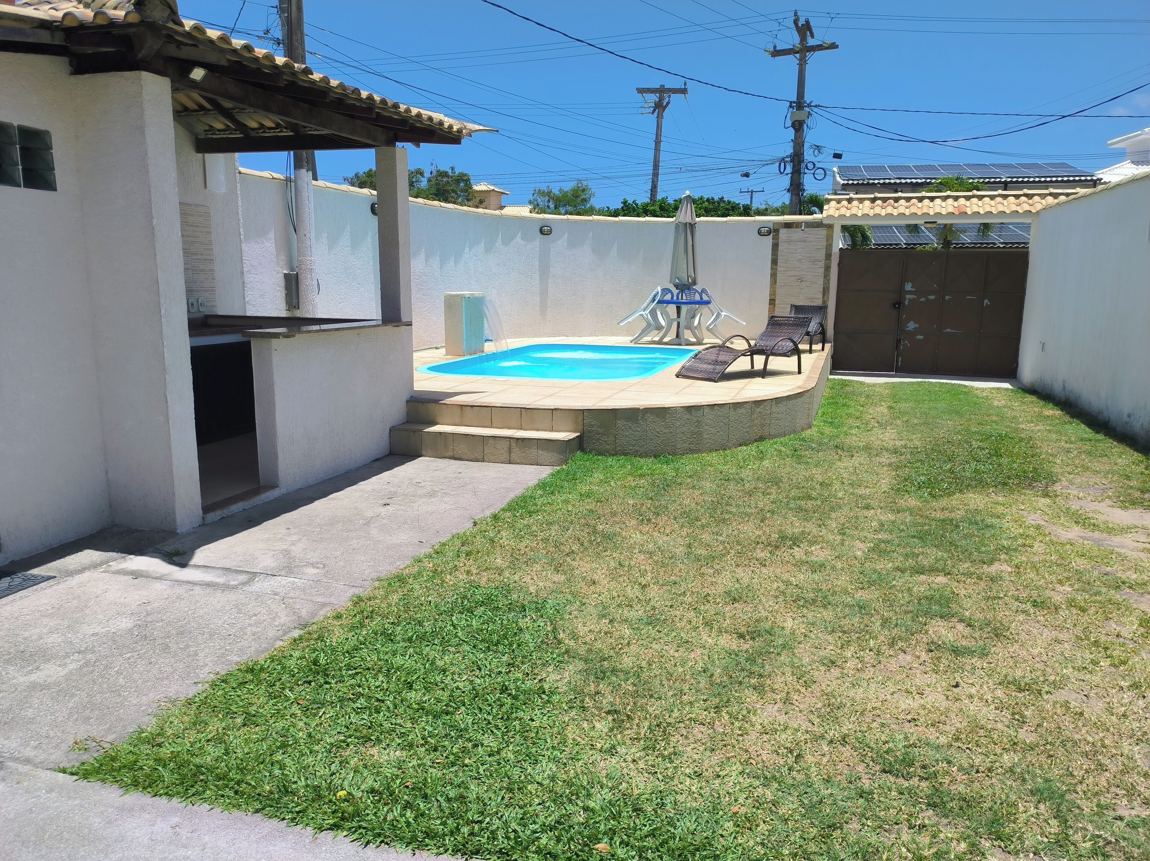 Um quintal com piscina, varanda coberta e uma mesa pequena com cadeiras.