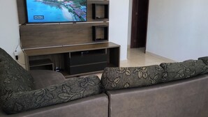 Una sala de estar moderna con un televisor de pantalla plana grande montado en un mueble bajo de madera, un sofá seccional gris con cojines estampados y piso de baldosas.