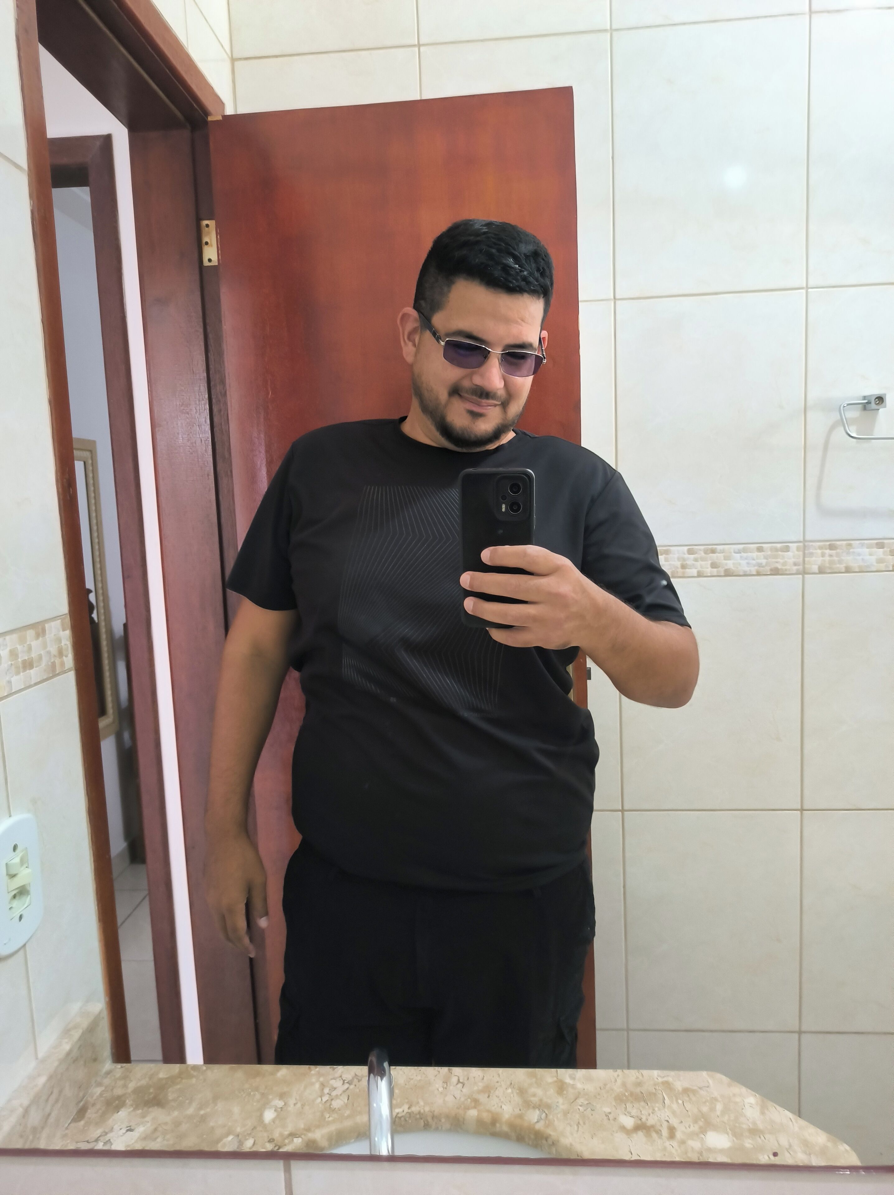 A man taking a selfie in a bathroom with a mirror, a sink, and a door.