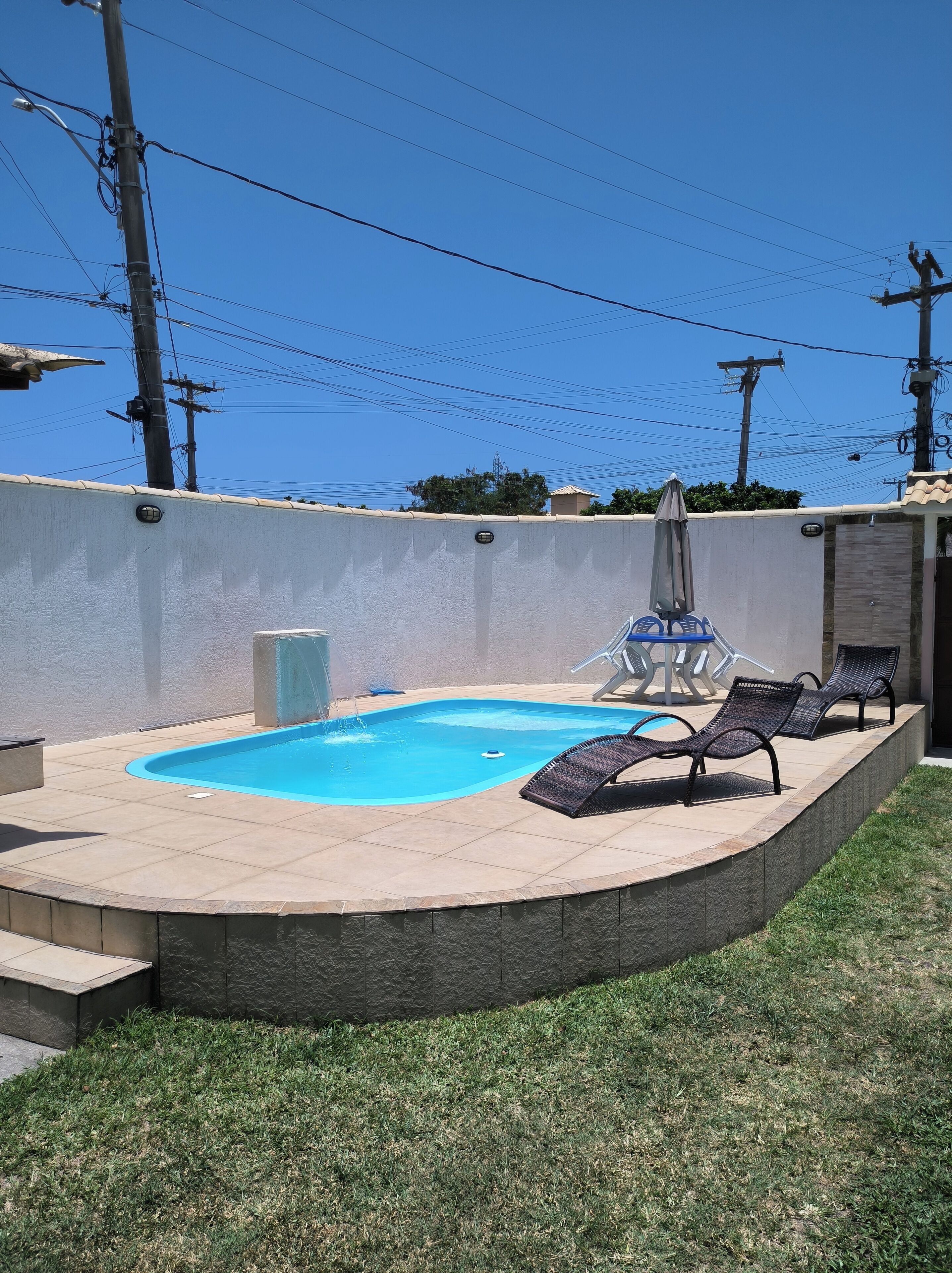 A swimming pool with a tiled deck, surrounded by a low stone wall, and equipped with lounge chairs.