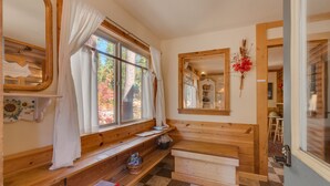 Una panca di legno, un pavimento a scacchi, una finestra con tende e uno specchio appeso al muro.