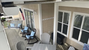 A covered patio with a table and chairs, a small seating area with a bench and cushions, and a window with a welcome sign. - CottageVacations4u "Beach Be With You"- ocean view- pool club-200 FT to beach! (Ocean Isle Beach)