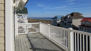 A wooden deck with a white railing, overlooking a beach and houses. - CottageVacations4u "Another Day at the Beach"-Ocean View- Pool Club-dog friendly (Ocean Isle Beach)