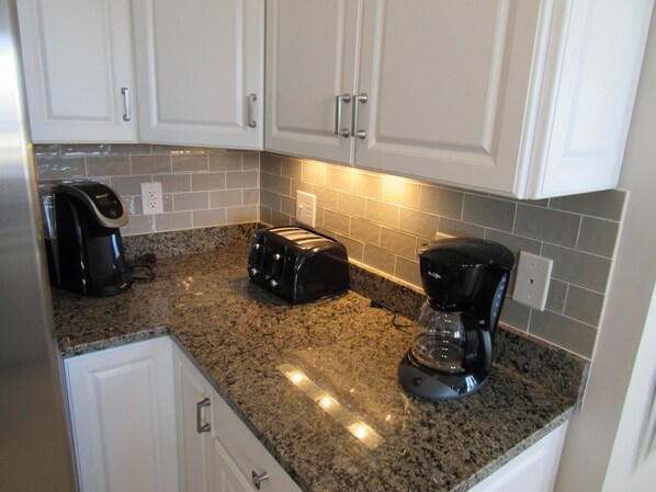 A kitchen with white cabinets, a granite countertop, and two coffee makers.