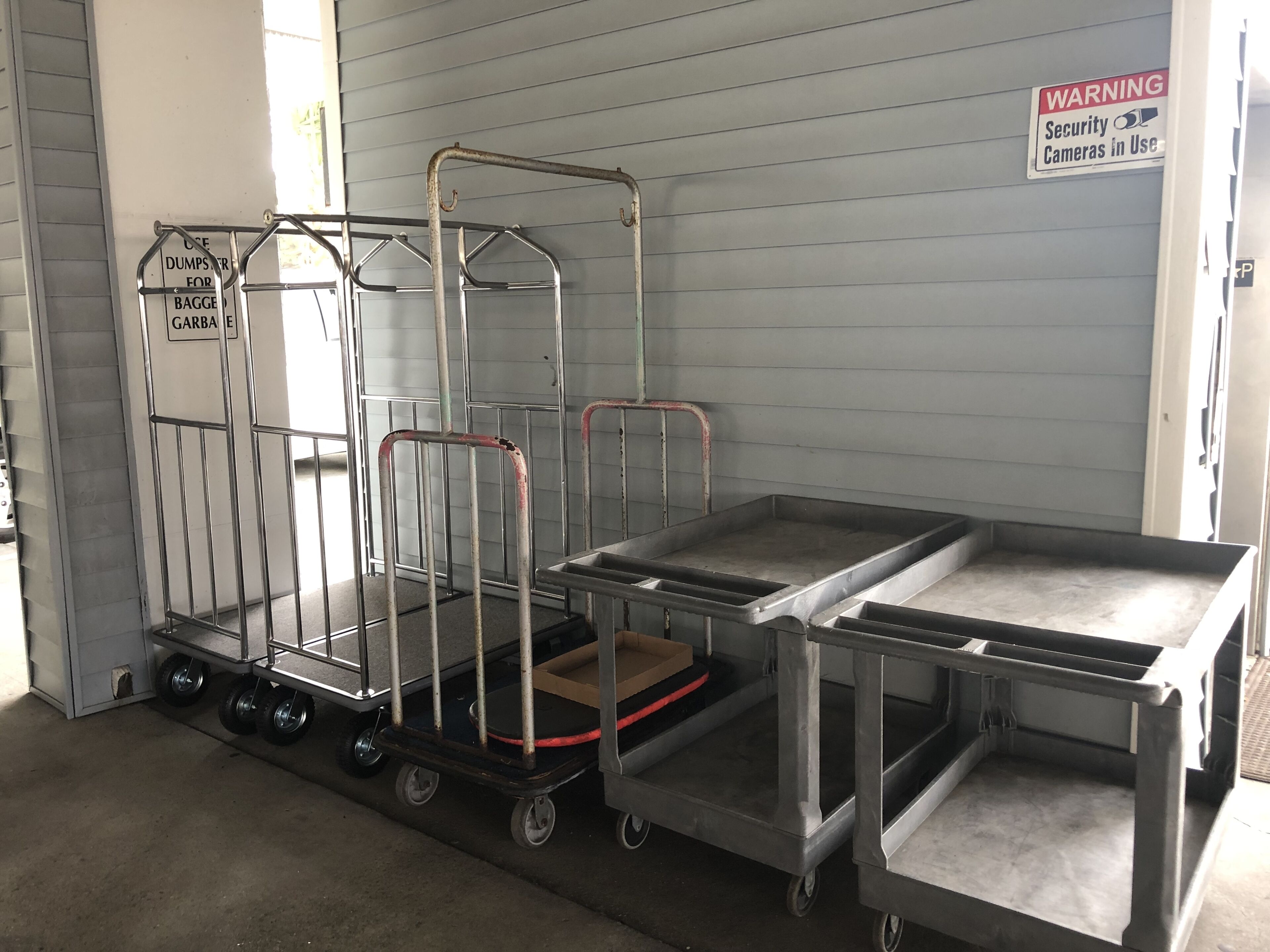 A metal cart with multiple compartments and wheels, placed indoors against a wall with a warning sign.