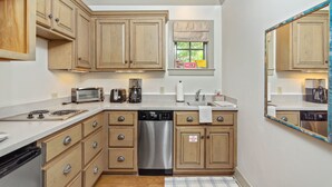 A compact kitchen with wooden cabinets, a dishwasher, a stove, and a window with a view of greenery. - Charming Carriage House located in Rosemary Beach ~ Pet Friendly (Rosemary Beach)