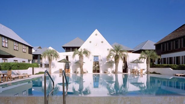 A hotel with a central pool, palm trees, and a white building with a triangular roof. - Charming Carriage House located in Rosemary Beach ~ Pet Friendly (Rosemary Beach)