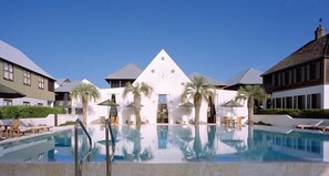 Un hôtel doté d’une piscine centrale, de palmiers et d’un bâtiment blanc surmonté d’un toit triangulaire.