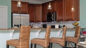A kitchen with wooden cabinets, a stainless steel refrigerator, a microwave, and a woven chair bar with four chairs. - Surfside Beach 5 Bdr, Walk 2 Beach, Priv Pool, Putt Green, Golf Cart (Surfside beach)