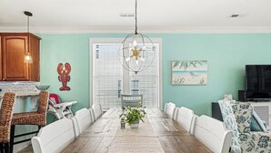 A dining area with a wooden table, white chairs, a hanging light fixture, and a potted plant. - Surfside Beach 5 Bdr, Walk 2 Beach, Priv Pool, Putt Green, Golf Cart (Surfside beach)