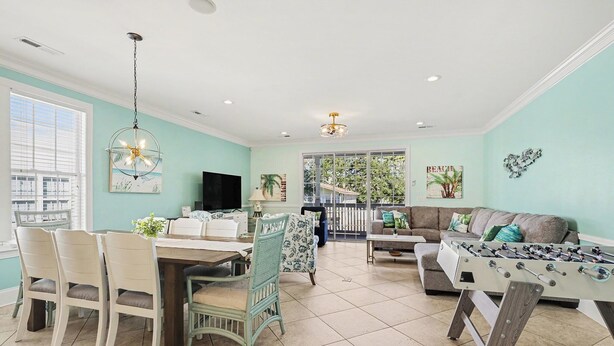 A spacious living room with a foosball table, a dining area with a table and chairs, and a large window providing natural light. - Surfside Beach 5 Bdr, Walk 2 Beach, Priv Pool, Putt Green, Golf Cart (Surfside beach)