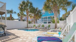 A pool area with lounge chairs, a pool, palm trees, and a building in the background. - Surfside Beach 5 Bdr, Walk 2 Beach, Priv Pool, Putt Green, Golf Cart (Surfside beach)