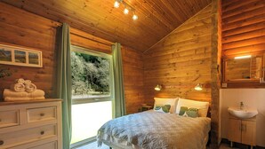 A wooden cabin bedroom with a bed, dresser, and a window with curtains. - Stylish, Comfy & Cosy log cabin in National Park, dogs & families welcome! (Rashfield (near Dunoon))