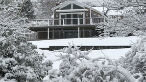 Una casa de dos pisos con balcón, rodeada de árboles cubiertos de nieve.