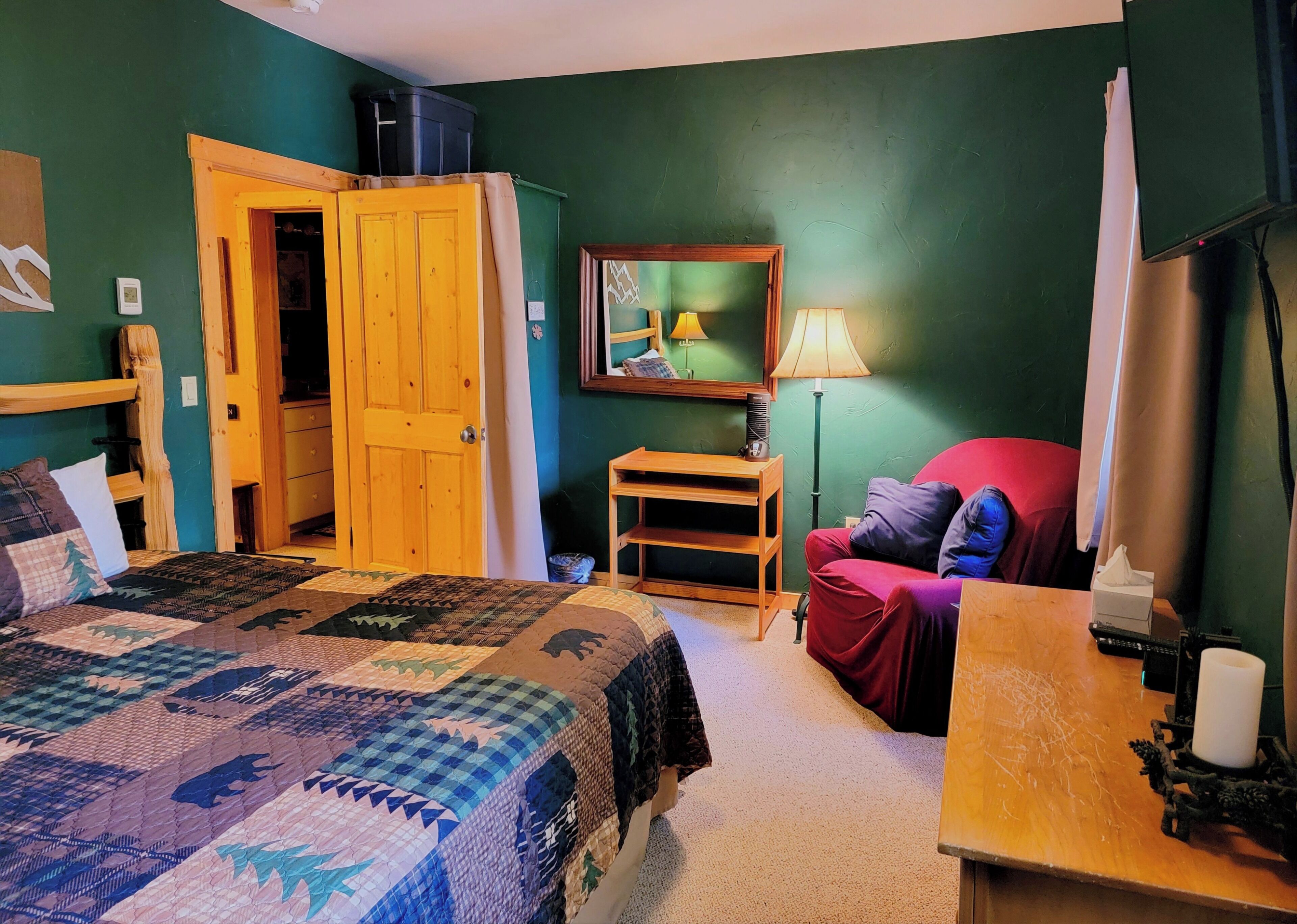 Une chambre confortable avec un grand lit, une table de chevet en bois, un fauteuil rouge et un bureau avec une lampe.