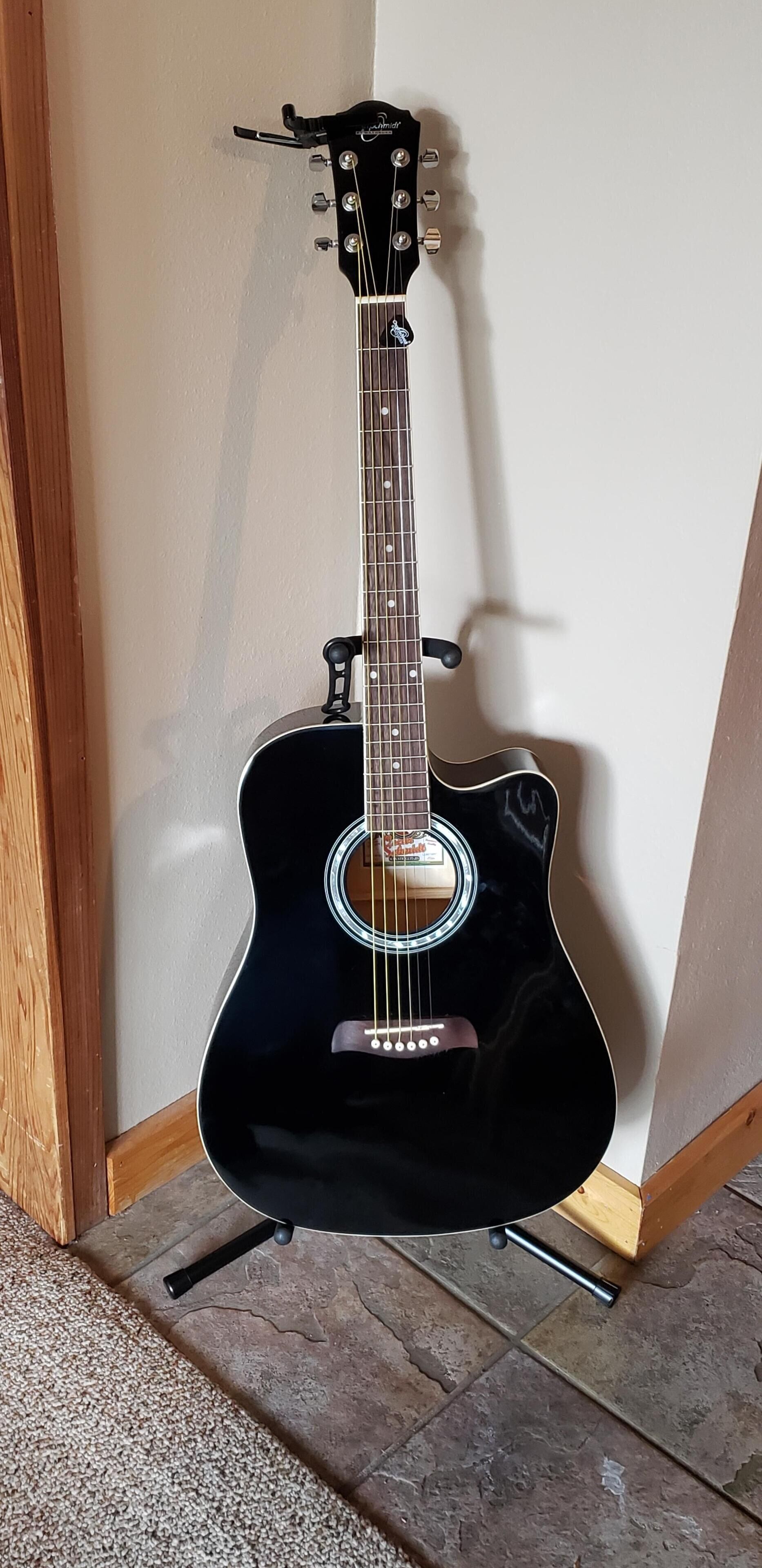 A black acoustic guitar leaning against a wall in a corner.