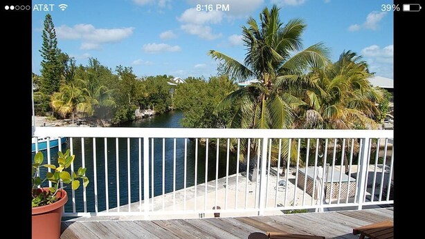 A balcony with a view of a river, palm trees, and a wooden deck. - Nader Vacation Rental (Little Torch Key)