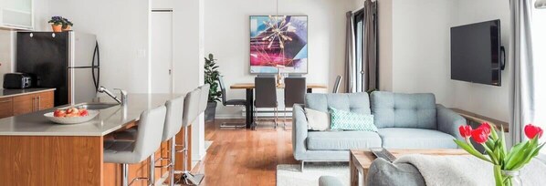 Una sala de estar moderna con un sofá, una mesa de comedor y una cocina con refrigerador y fregadero.