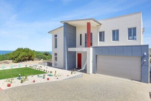 Una casa moderna de dos pisos con garaje, una puerta roja y un jardín delantero ajardinado.