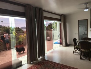 A spacious living area with a large sliding glass door leading to a balcony, a dining area with wooden chairs, and a ceiling fan. - Studio apartment 150 meters from the beach. (Ubatuba)