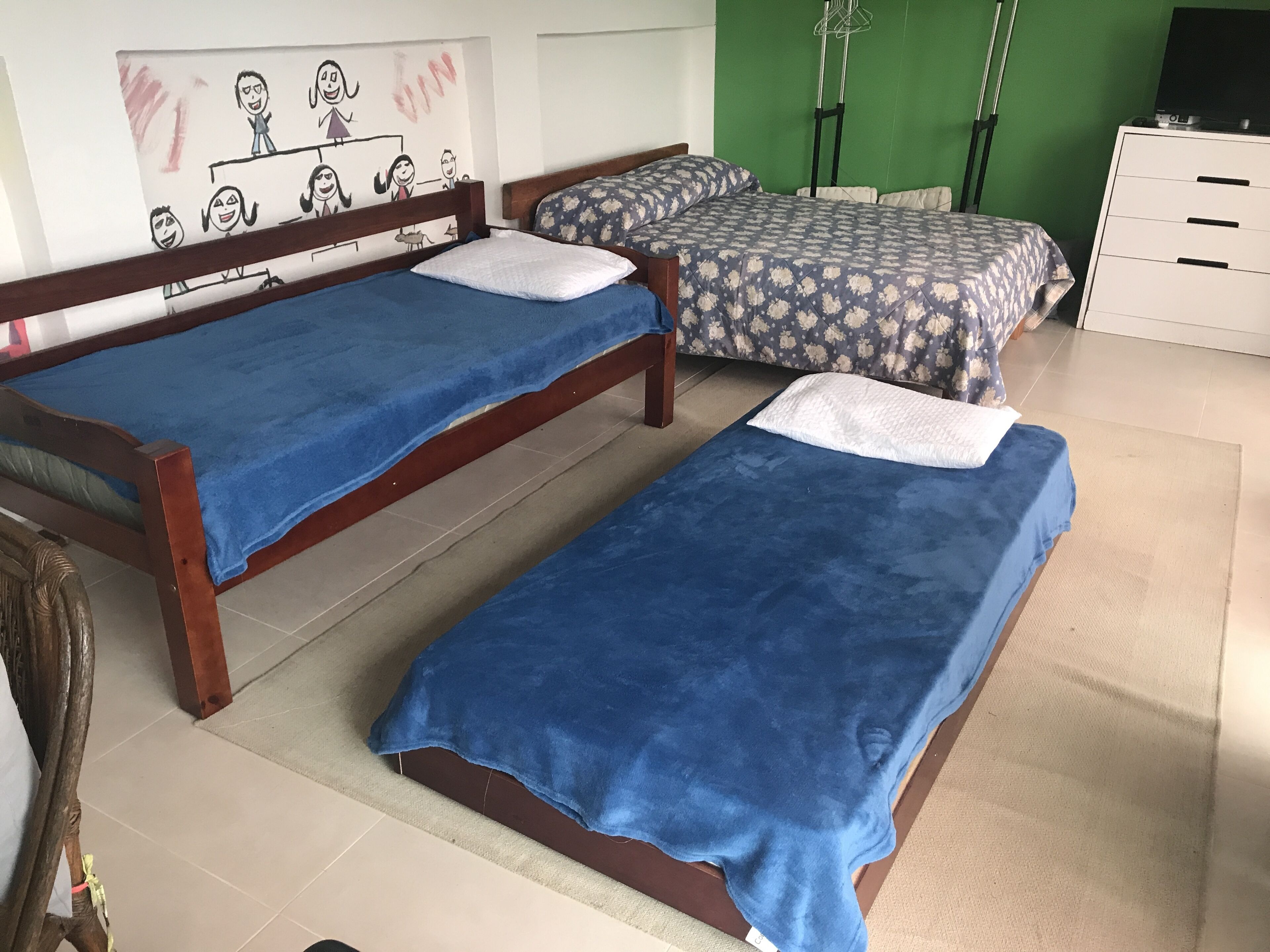 Une chambre à coucher avec deux lits en bois, un mur vert et une commode blanche.