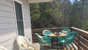 A wooden deck with wicker chairs and a table, a colorful crocheted blanket, and a view of trees.
