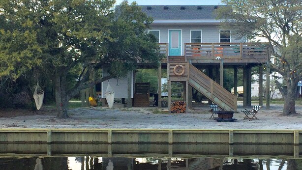 A waterfront house with a wooden deck, a slide, and a small dock extending into the water.