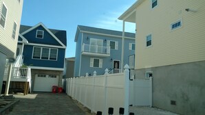 Un barrio residencial con una casa azul, una casa color beige y una cerca blanca.