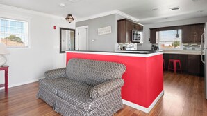 Una cocina moderna con una isla roja, un sofá gris y suelo de madera.