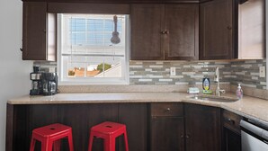 Una cocina con armarios de madera oscura, un ventanal con persianas, una cafetera y dos taburetes rojos.