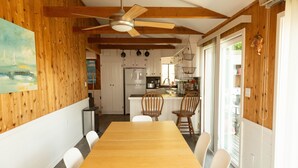 Un coin repas avec une table et des chaises en bois, un ventilateur de plafond et une cuisine en arrière-plan.
