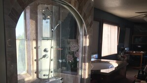 A bathroom with a glass-enclosed shower, a vanity with a mirror, and a window.